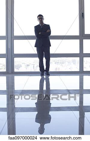 Businessman learning against high rise window, backlit by sunset glow View Large Photo Image Picture - Businessman learning against high rise window, backlit by sunset glow. Fotosearch