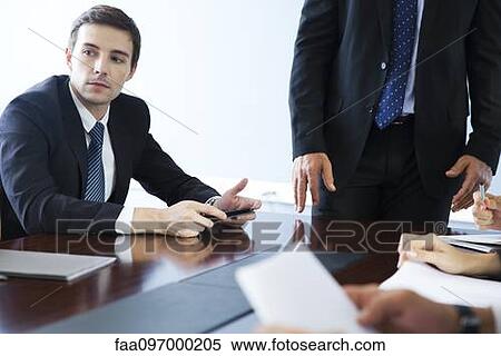 Stock Photography - Businessman listening to collegues speak during meeting. Fotosearch