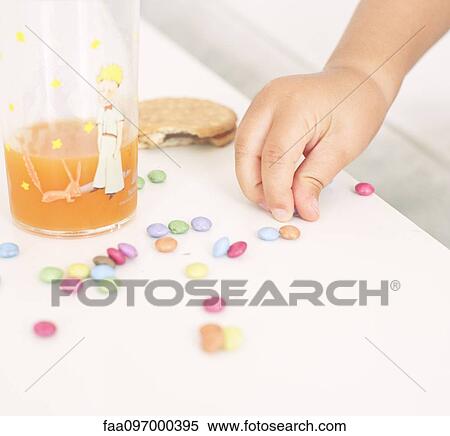 Stock Photography - Child picking up candies from table. Fotosearch