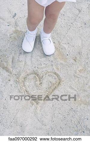 Stock Image - Child standing over heart drawn in sand. Fotosearch
