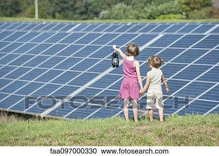 Stock Image - Children standing together in front of solar panels, girl holding old-fashioned latern. Fotosearch