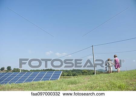 Stock Image - Children walking in field near solar panels and power lines, carrying old-fashioned lantern. Fotosearch