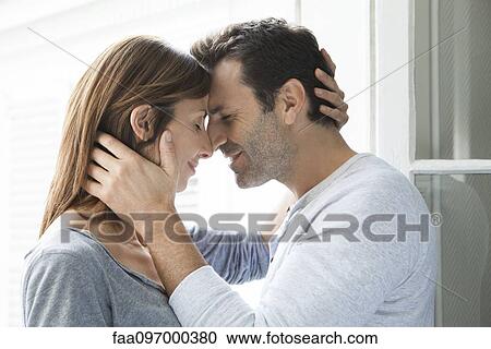 Stock Image - Couple cuddling by open window. Fotosearch