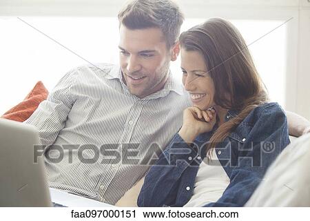 Stock Image - Couple relaxing at home looking at laptop computer together. Fotosearch