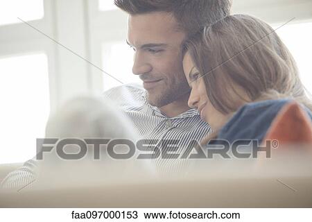Stock Image - Couple relaxing at home looking at laptop computer together. Fotosearch