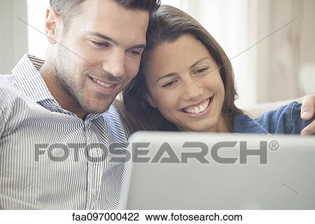 Stock Image - Couple relaxing at home looking at laptop computer together. Fotosearch