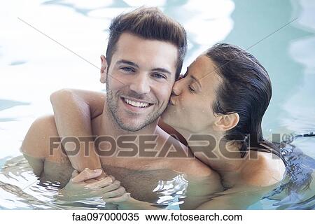 Couple relaxing together in pool, woman kissing man's cheek View Large Photo Image Stock Photography - Couple relaxing together in pool, woman kissing man's cheek. Fotosearch