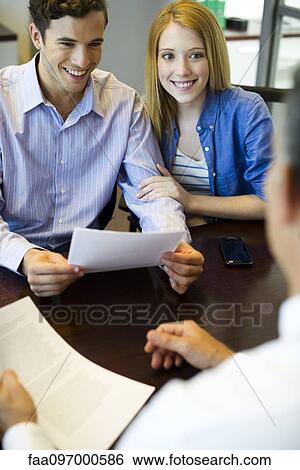 Stock Photograph - Couple reviewing paperwork in meeting with advisor. Fotosearch