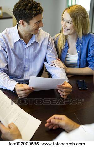 Stock Photography - Couple reviewing paperwork in meeting with advisor. Fotosearch