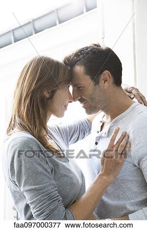 Stock Photo - Couple touching noses and embracing by open window. Fotosearch
