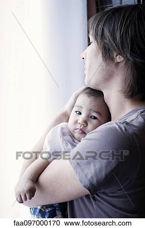 Stock Image - Father holding baby, looking out window. Fotosearch