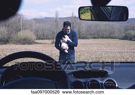 Stock Photograph - Father holding baby, seen through car windshield. Fotosearch