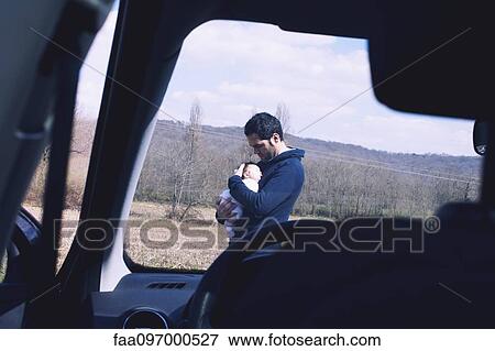 Stock Photo - Father holding baby, viewed through car windshield. Fotosearch