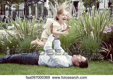 Father lying on grass, playfully lifting young daughter in air View Large Photo Image Stock Photo - Father lying on grass, playfully lifting young daughter in air. Fotosearch