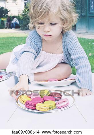 Picture - Little girl choosing macaroon from plate. Fotosearch
