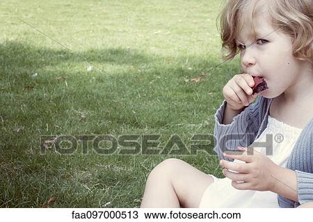 Stock Image - Little girl eating sweet snack outdoors. Fotosearch