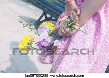 Stock Photo - Little girl holding flowers behind her back. Fotosearch