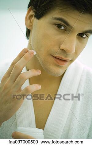 Stock Image - Man in bathrobe moisturizing face. Fotosearch