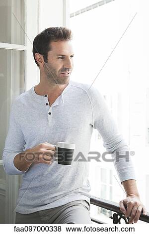 Stock Photo - Man looking out of window with mug in hand. Fotosearch