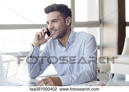 Stock Image - Man making cell phone call while using laptop computer. Fotosearch