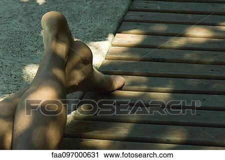 Stock Image - Man reclining on deck, legs crossed at ankle, cropped. Fotosearch