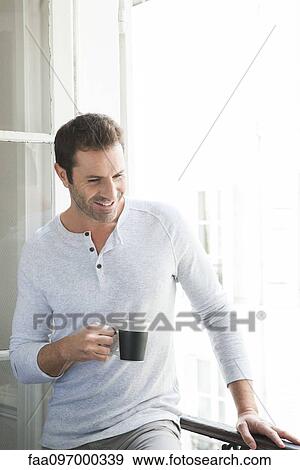 Stock Photo - Man standing by window with mug in hand. Fotosearch