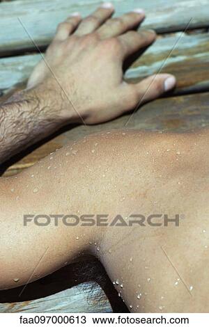 Stock Image - Man's wet shoulder and hand on wooden deck. Fotosearch