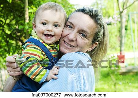 Stock Photo - Mother holding baby outdoors, both smiling, portrait. Fotosearch