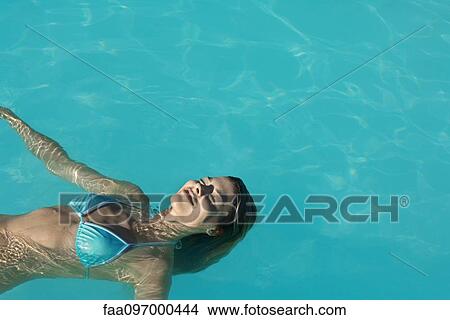 Picture - Woman floating in pool, eyes closed, high angle view. Fotosearch