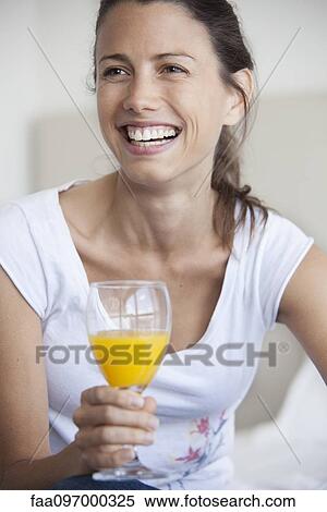 Stock Photography - Woman holding glass of juice, smiling cheerfully. Fotosearch