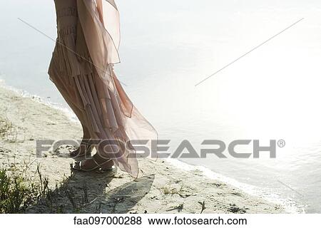 Stock Photo - Woman in dress walking along shore, low section. Fotosearch