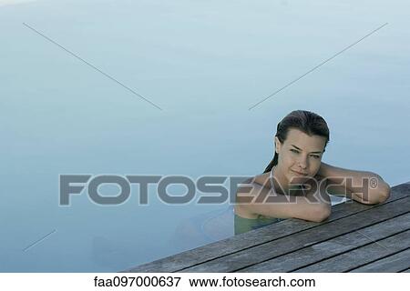 Stock Photo - Woman in pool leaning against deck, looking at camera. Fotosearch