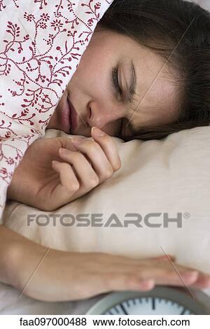 Stock Photo - Woman lying in bed, silencing alarm clock. Fotosearch