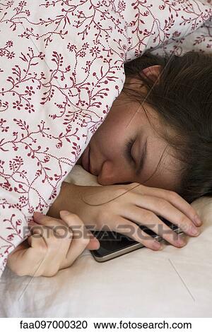 Stock Image - Woman sleeping in bed with smartphone in hand. Fotosearch