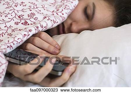 Stock Image - Woman sleeping in bed with smartphone in hand. Fotosearch