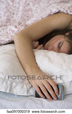 Woman sleeping in bed with smartphone in hand View Large Photo Image Stock Photo - Woman sleeping in bed with smartphone in hand. Fotosearch
