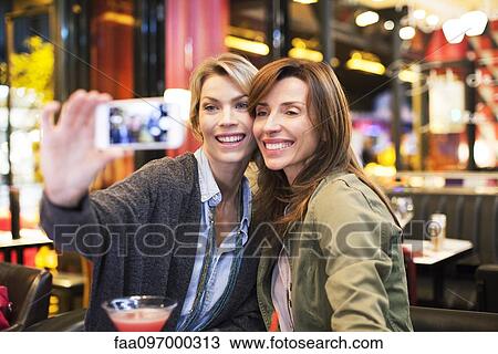 Stock Image - Women in bar taking self-portrait with photophone. Fotosearch