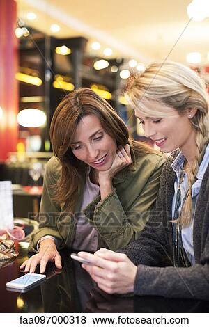 Stock Photo - Women looking down at cell phone together. Fotosearch