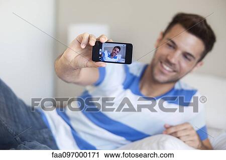 Young man reclining on bed taking selfie with smartphone View Large Photo Image Stock Image - Young man reclining on bed taking selfie with smartphone. Fotosearch