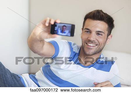 Young man reclining on bed taking selfie with smartphone View Large Photo Image Stock Image - Young man reclining on bed taking selfie with smartphone. Fotosearch