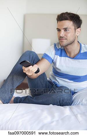 Young man reclining on bed watching tv View Large Photo Image Stock Image - Young man reclining on bed watching tv. Fotosearch