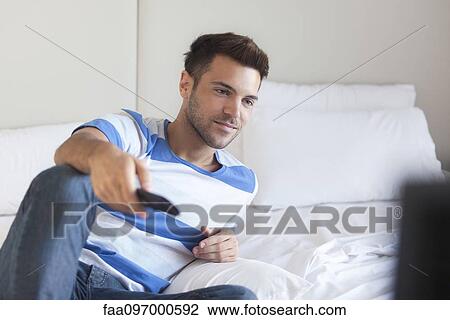 Young man reclining on bed watching tv View Large Photo Image Stock Image - Young man reclining on bed watching tv. Fotosearch