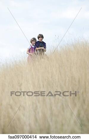 Young siblings walking together through tall grass View Large Photo Image Picture - Young siblings walking together through tall grass. Fotosearch