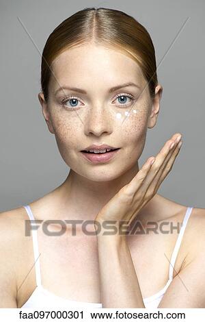 Stock Image - Young woman applying moisturizer to face. Fotosearch