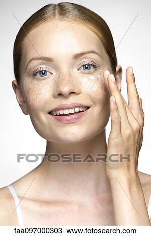 Stock Image - Young woman applying undereye cream. Fotosearch