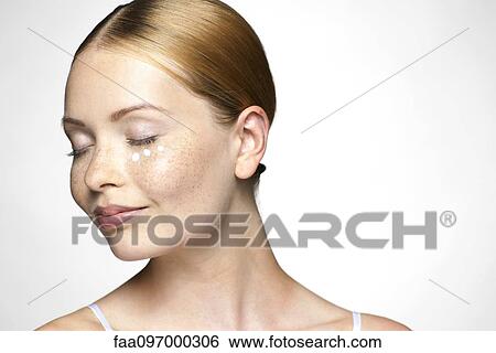 Stock Photograph - Young woman applying undereye cream. Fotosearch