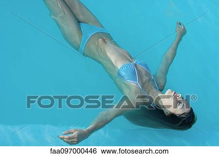 Stock Photograph - Young woman floating in swimming pool, eyes closed. Fotosearch