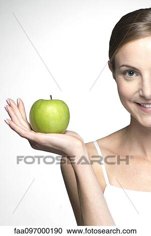 Stock Image - Young woman holding up green apple. Fotosearch