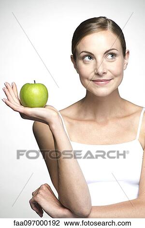 Stock Image - Young woman holding up green apple. Fotosearch