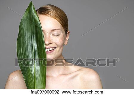 Young woman holding up leaf concealing part of face View Large Photo Image Stock Image - Young woman holding up leaf concealing part of face. Fotosearch